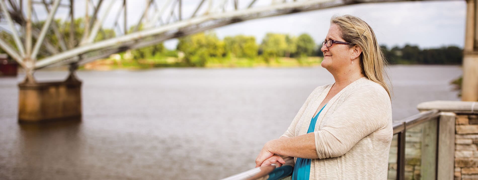 Bir nehrin üzerinden bakan bir köprünün yanında duran bir kadın.