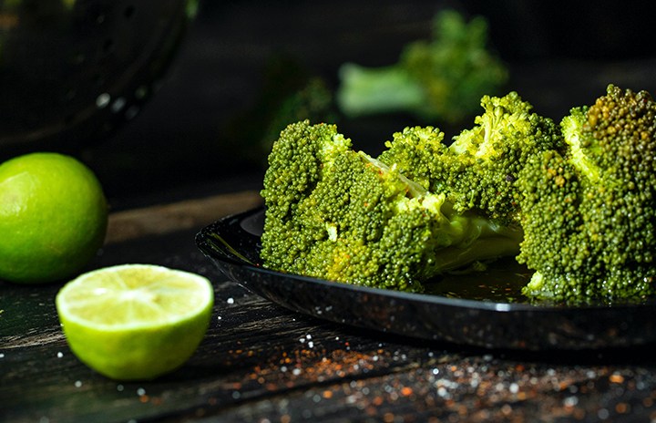 A couple of broccoli on a plate with limes laying next to it.